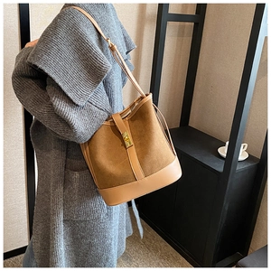 Detail view of brown suede bucket bag with metal turn-lock closure on model shoulder
