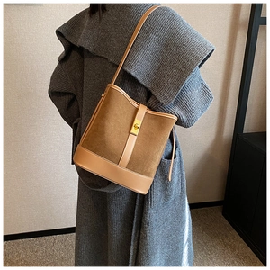 Close-up of brown suede bucket bag featuring a gold turn-lock closure on grey coat
