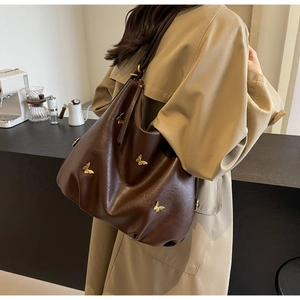 Detail of a large brown PU leather tote bag featuring gold butterfly metal decorations