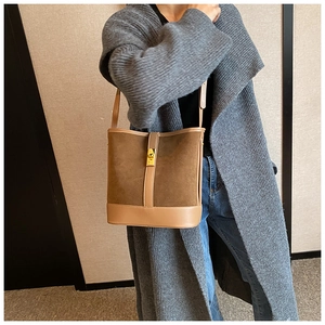 Brown faux suede bucket bag with gold twist lock shown on a model in a minimalist setting