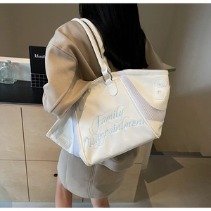 Detail of white nylon tote bag featuring blue embroidery and mesh side panels