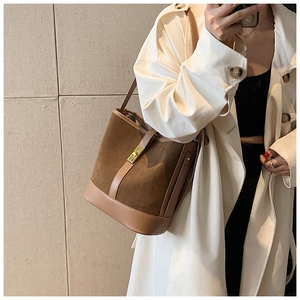 Close-up of brown suede bucket bag with gold metal swivel lock on a model coat