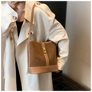 Detail of a brown faux suede bucket bag with gold twist lock on a white trench coat