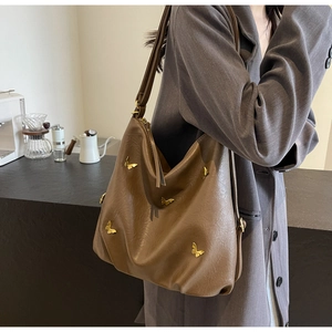 Brown PU leather tote bag with gold butterfly accents worn by a model in a café setting