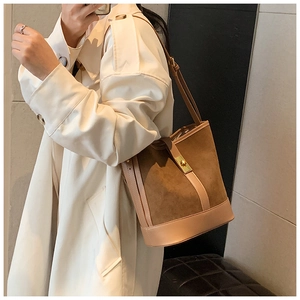 Detail of brown suede bucket bag with gold clasp and leather stitching on model