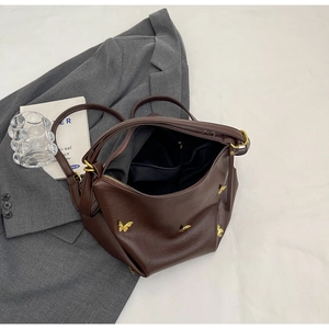 Detail view of dark brown PU leather handbag with golden butterfly ornaments on a blazer