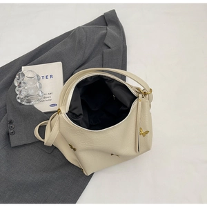 Detail view of beige PU shoulder bag interior with golden butterfly accent and black lining