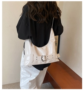 Side view of a large cream white patent leather hobo bag worn by a model in a minimal room