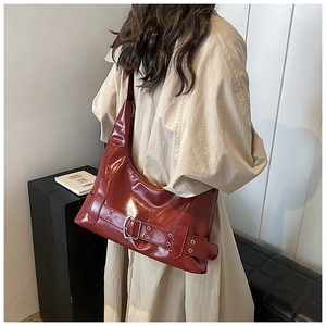 Macro shot of glossy dark red patent leather shoulder bag with silver buckle details