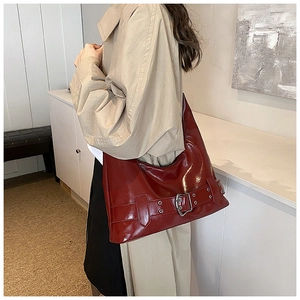 Detail view of deep red shiny leather shoulder bag with metallic buckle on a model