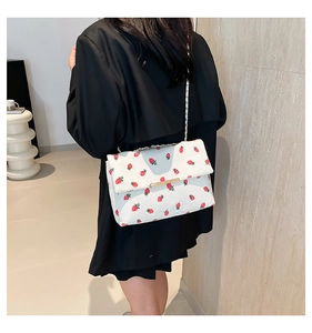 Detail of strawberry print corduroy crossbody bag worn by a model in black blazer