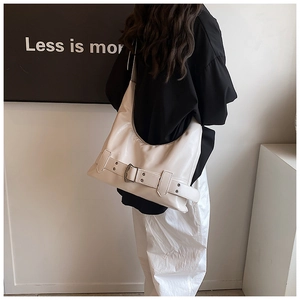 Minimalist beige leather shoulder bag with decorative buckle shown in an artistic setting