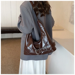 Detail of a large glossy faux leather hobo bag in deep reddish brown with metal buckle belt