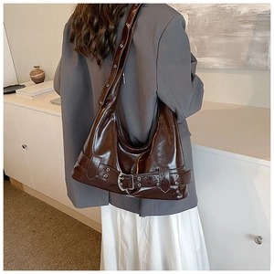 Close-up of chocolate brown patent leather shoulder bag with silver eyelets and buckles