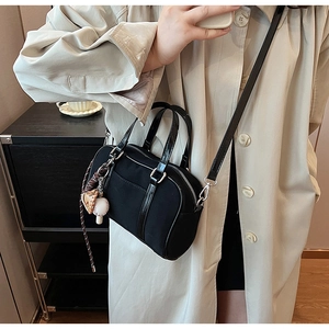 Dettaglio della borsa bowling in tela nera con manici lucidi su cappotto beige