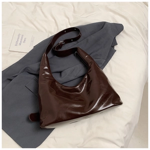 Deep brown glossy leather hobo bag with adjustable strap on a grey suit background