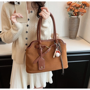 Detailaufnahme der braunen Wildledertasche mit Lederbesatz, Schnalle und Baseball-Anhänger