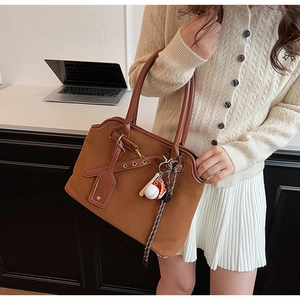 Details einer braunen Wildleder-Schultertasche mit Lederriemen und Baseball-Anhängern