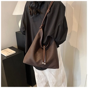 Detail of a dark brown shoulder bag with knotted strap and metal bead drawstring design