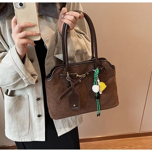Detail der dunkelbraunen Wildleder-Handtasche mit Trapezform und grünem Anhänger