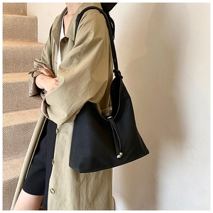 Detail of minimalist black PU tote bag showing knotted shoulder strap and side drawstring cord