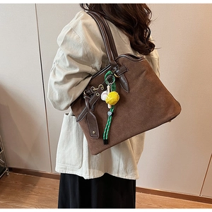 Detail einer großen Wildleder-Tote-Bag mit braunen Ledergriffen und Sportanhänger