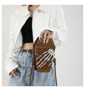 Detailed close-up of coffin-shaped brown PU leather bag with embossed skulls and 3D skeleton hand