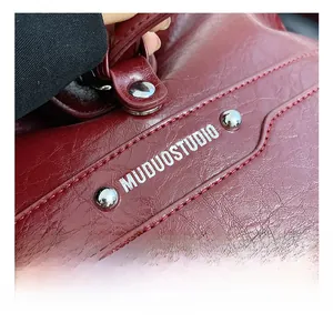 Detail of burgundy vintage oil wax leather bag with silver rivets and branding