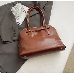 Detail der karamellbraunen PU-Ledertasche mit Metallnieten auf dunkelgrauem Anzug