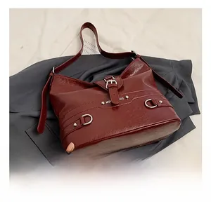 Detail view of burgundy leather shoulder bag with silver hardware on blazer background