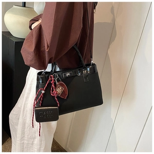 Detail of black PU tote bag with glossy trim, metal twist lock and red braided charm