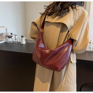 Detail of deep red PU leather hobo bag with gold zipper held by a model in a trench coat