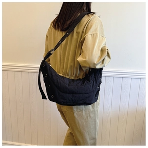 Detail view of a black crescent nylon crossbody bag with eyelet decor on model