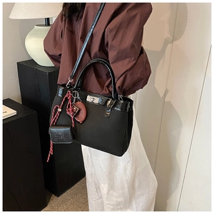 Detail of black mixed-material handbag with silver twist lock and multiple decorative charms