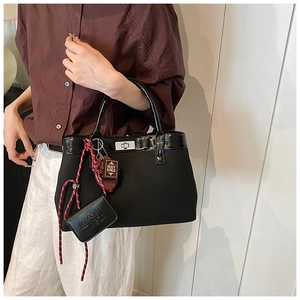 Detail of black tote bag with silver twist lock and decorative bible pendant