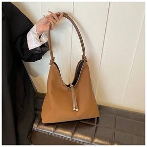 Detail of caramel brown PU leather tote bag with metal ball drawstring on a leather bench