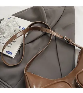 Detail view of brown PU leather crescent shoulder bag with silver zipper on grey blazer