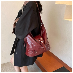Detail of burgundy waxed leather shoulder bag with silver hardware on a female model