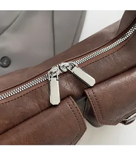 Detail einer braunen PU-Ledertasche mit Lychee-Struktur und glatten silbernen Reißverschlüssen