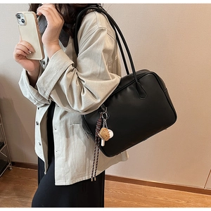 Détail d'un sac cabas noir en similicuir avec charm tressé porté par un mannequin chic