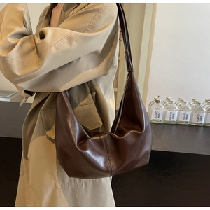 Brown moon-shaped PU leather bag detail shown on a trench coat model in a studio set