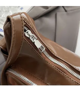 Detail of smooth silver zipper and glossy brown faux leather texture on the handbag