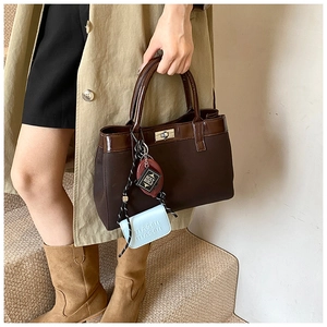 Detail of a brown PU tote bag featuring canvas texture, silver twist lock and custom charms