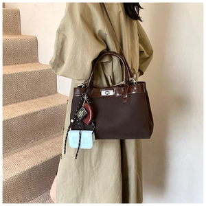 Close-up of dark brown tote bag with silver metal twist lock and decorative charms