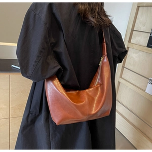 Brown faux leather hobo bag with glossy finish shown on shoulder in stylish setting