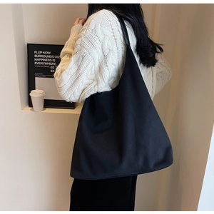 Minimalist black suede tote bag shown on model wearing a beige knitted sweater