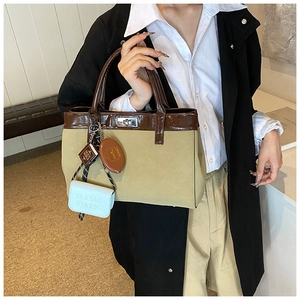 Detail of a beige PU tote bag featuring dark brown leather trim and metallic twist lock clasp