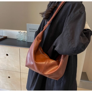 Detail of a brown caramel leather half-moon hobo bag worn over the shoulder by a model