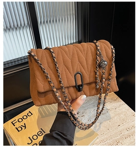 Detailed close-up of brown suede crossbody bag with V-quilted texture and metal lock