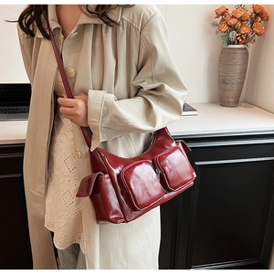 Detail of burgundy PU leather crossbody bag with multiple zip pockets on beige coat